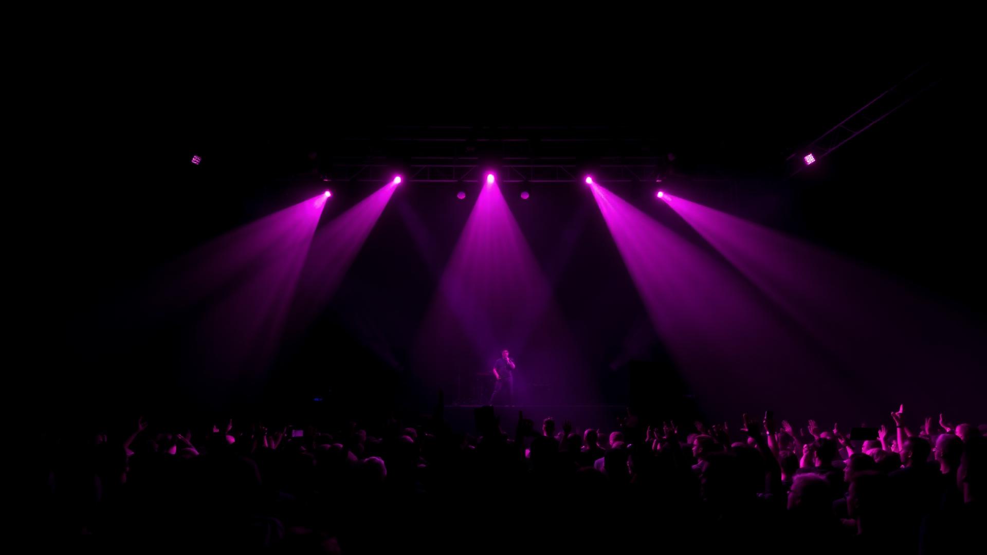 Escenario con luces moradas y público levantando las manos